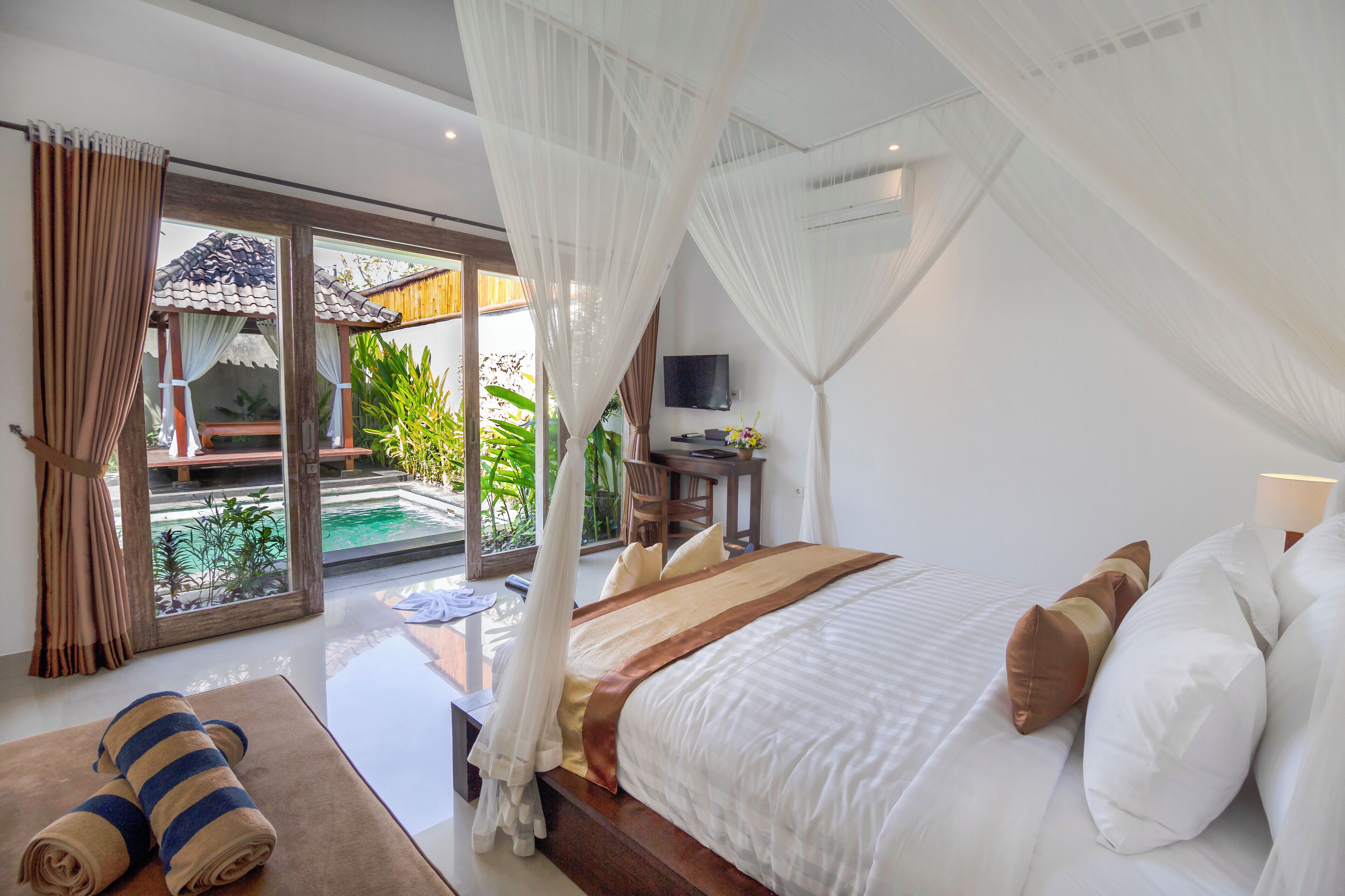 A bedroom with a large bed, a desk, and a view of a pool and greenery.