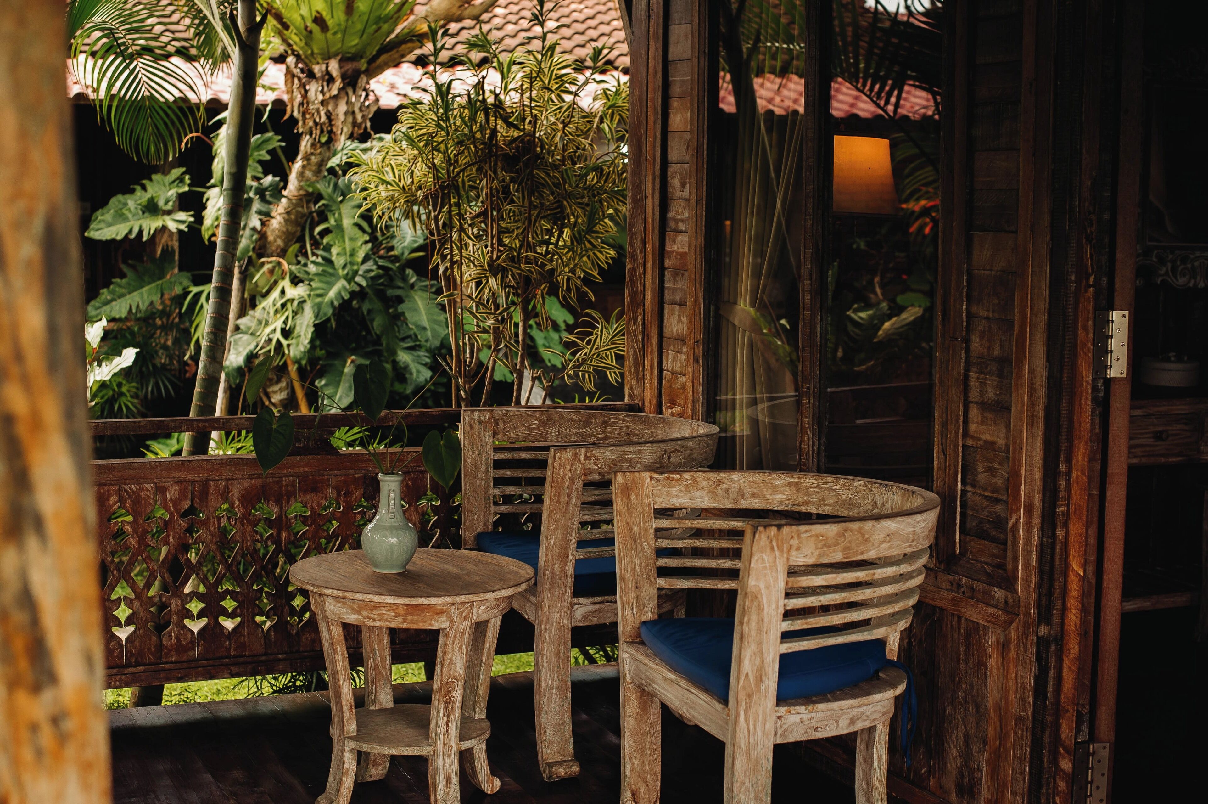 A wooden outdoor seating area with a table and chairs, surrounded by lush greenery and a wooden fence.