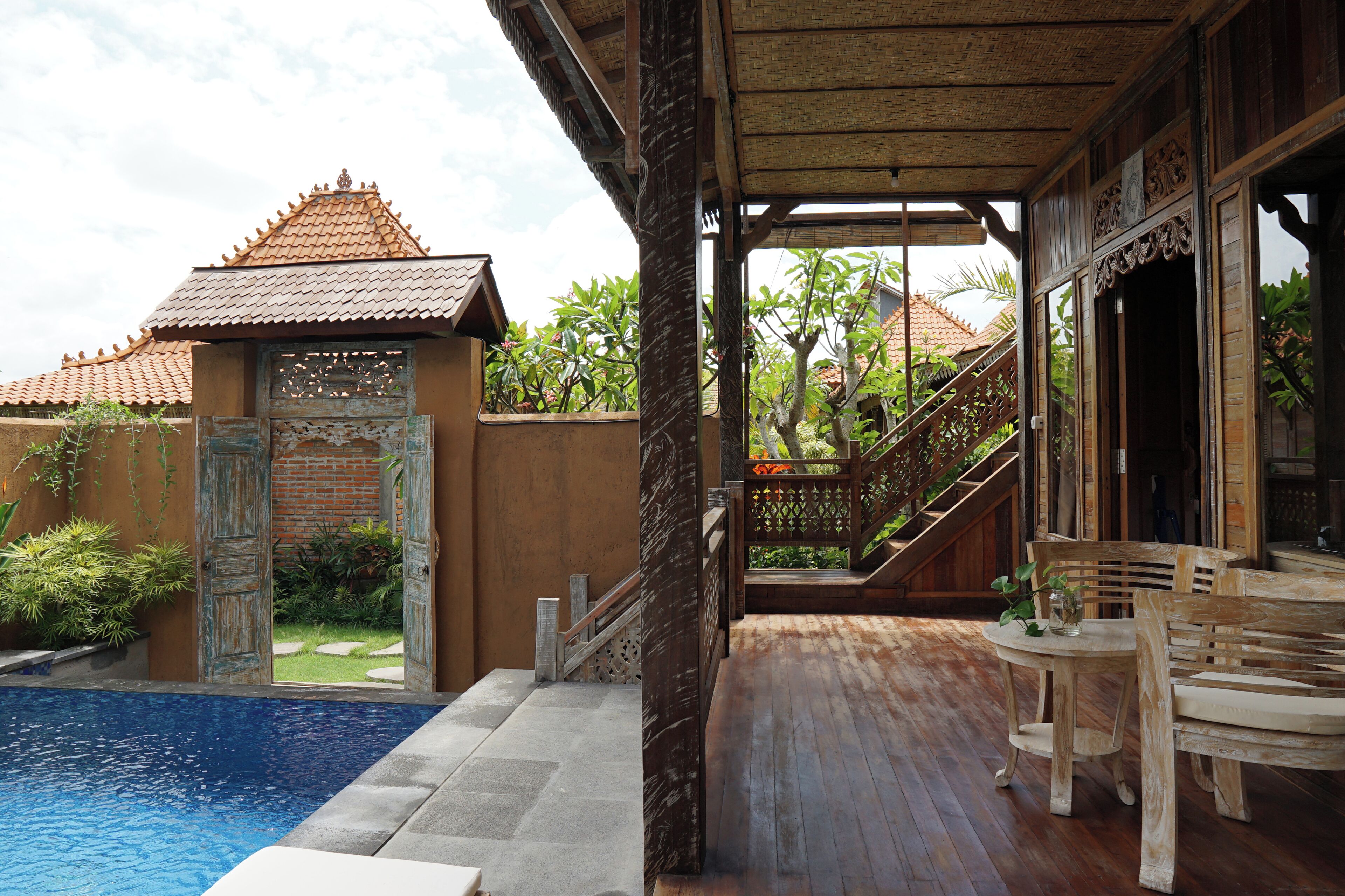 A wooden deck with a pool, a staircase, and a view of a traditional building with a tiled roof.