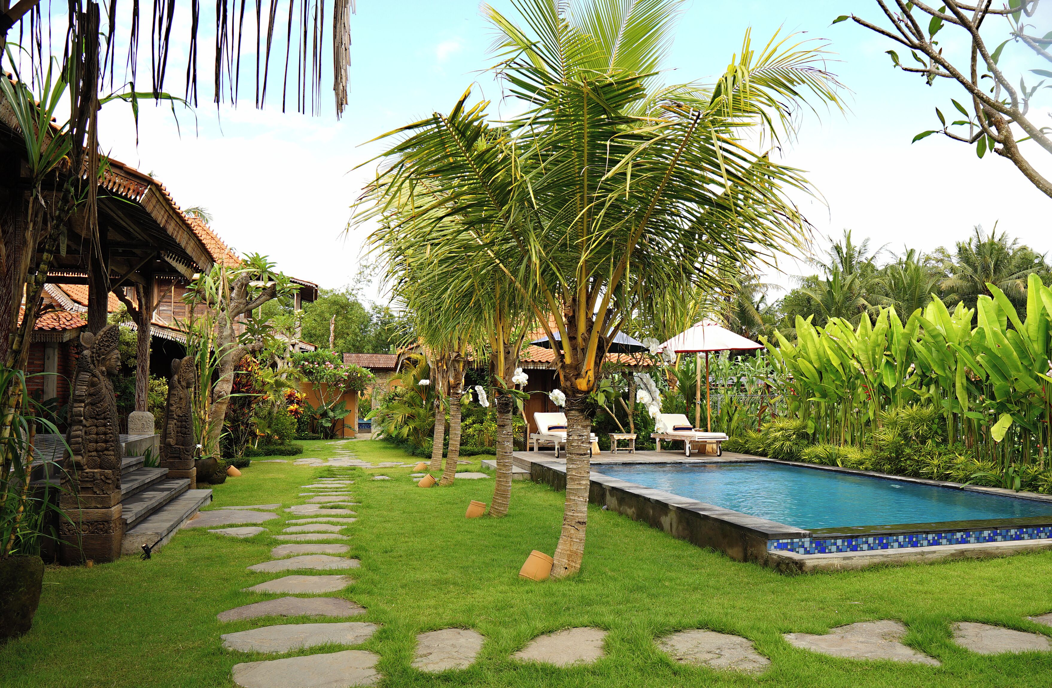 A pool area with a stone pathway, palm trees, and a tiled pool edge.