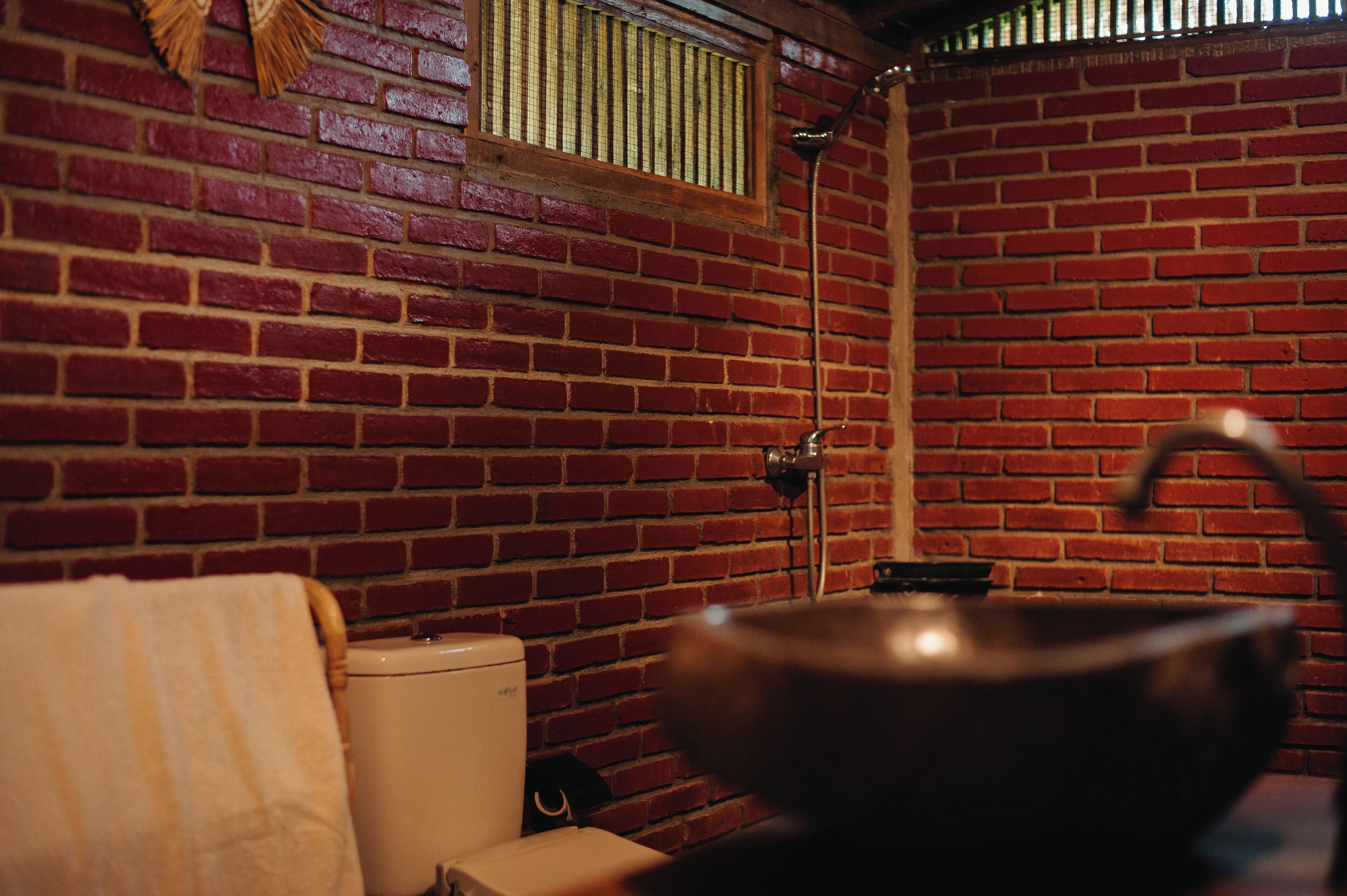 Ein Badezimmer mit Backsteinwand, Toilette, Waschbecken mit großer Schüssel und einem Handtuch an der Wand.