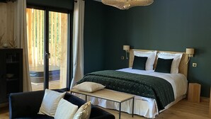 A bedroom with a large bed, a dark blue sofa, a wooden floor, and a large window with curtains.