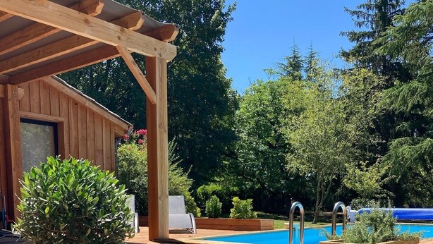 A wooden deck with a pool, surrounded by mulch and rocks.