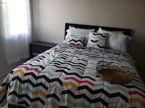 A neatly made bed with a chevron-patterned bedspread, two pillows with a chevron design, and a woven basket on the bed.