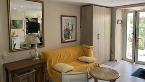 Ein Wohnzimmer mit einem gelben Sofa, einem Holztisch, einem Stuhl, einem großen Spiegel und einem Kleiderschrank.