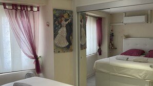 Ein Hotelzimmer mit Bett, Fenster mit durchsichtigen Vorhängen, einem Gemälde an der Wand und einem Spiegel.