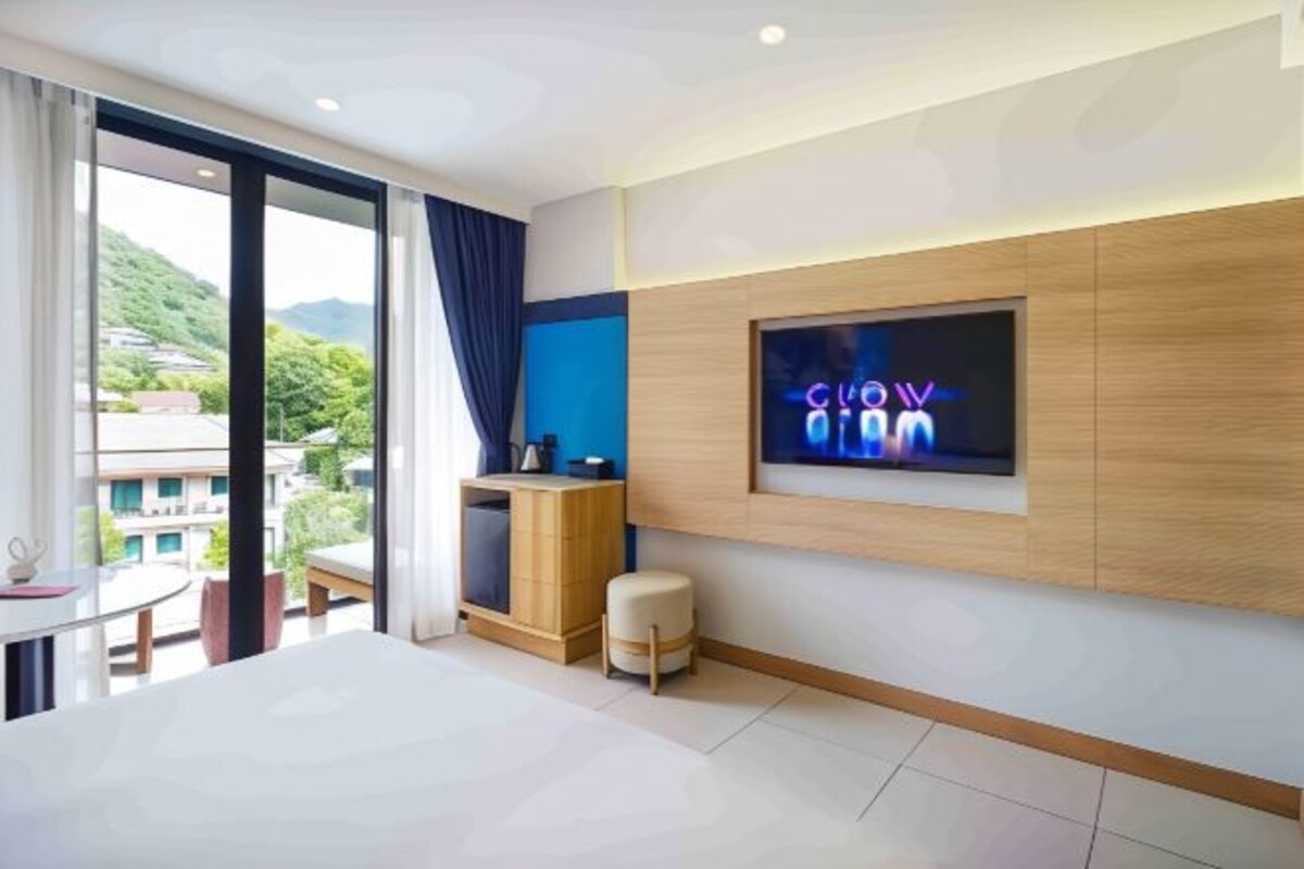 A modern hotel room with a large bed, a TV mounted on the wall, and a view of the cityscape through the window.