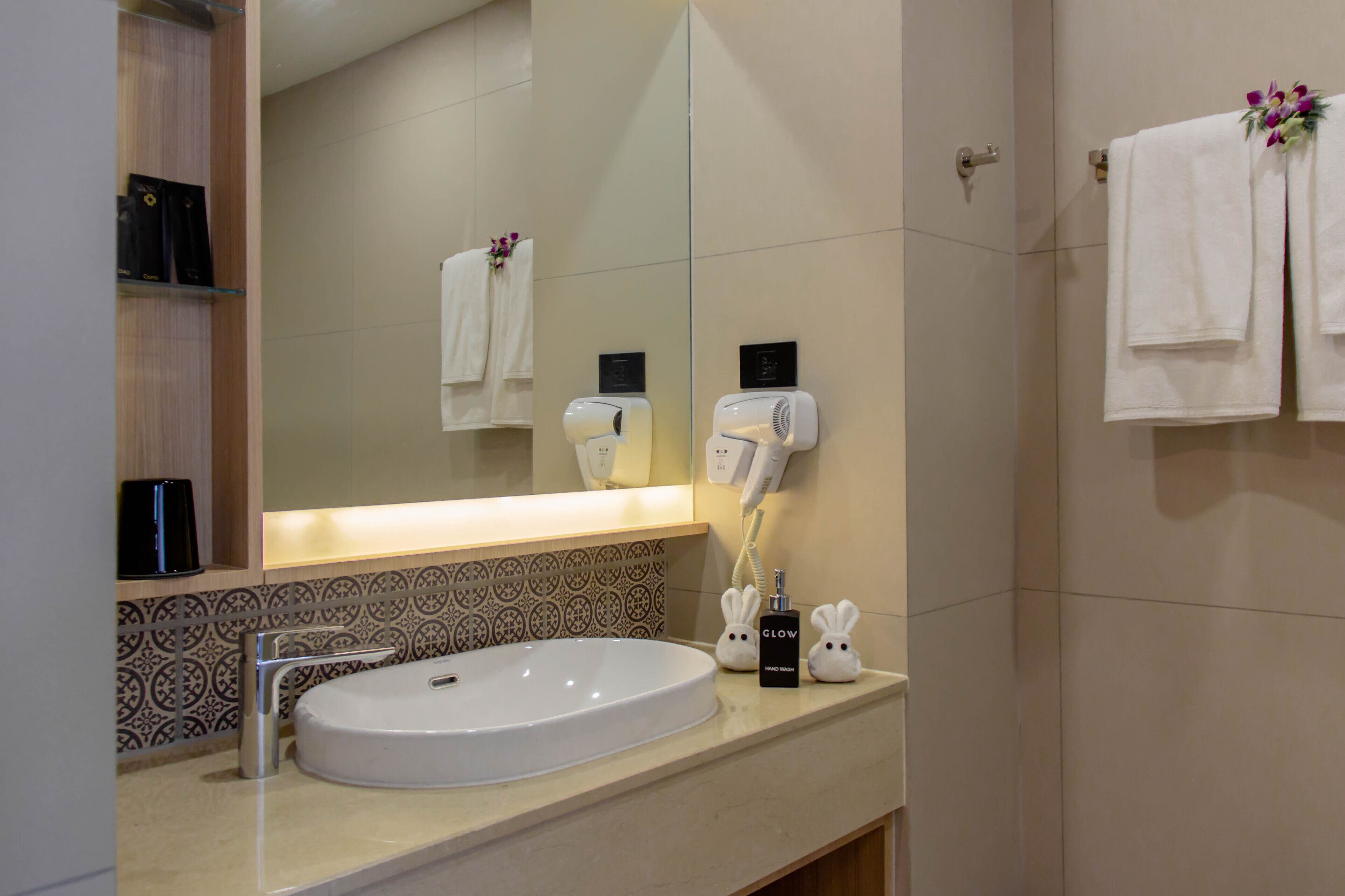 A bathroom with a white sink, a mirror, a hairdryer, and two towels hanging on the wall.