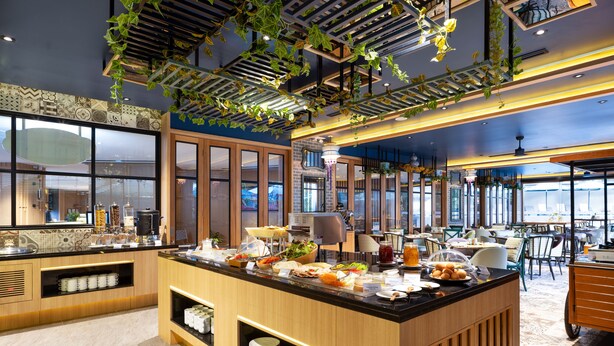 A modern kitchen with a central island, wooden cabinets, and hanging plants. - GLOW Mira Karon Beach (Karon)