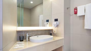 A modern bathroom with a large mirror, a sink, a hairdryer, and a trash bin.