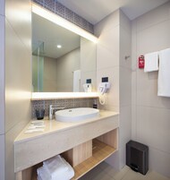 A modern bathroom with a large mirror, a sink, a hairdryer, and a trash bin.