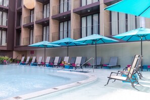 A pool area with lounge chairs and umbrellas, surrounded by a building with multiple floors and large windows. - GLOW Mira Karon Beach (Karon)