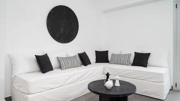 Un sofá modular blanco con cojines de estampado blanco y negro, una obra de arte circular negra en la pared y una mesa de centro negra con dos jarrones blancos.