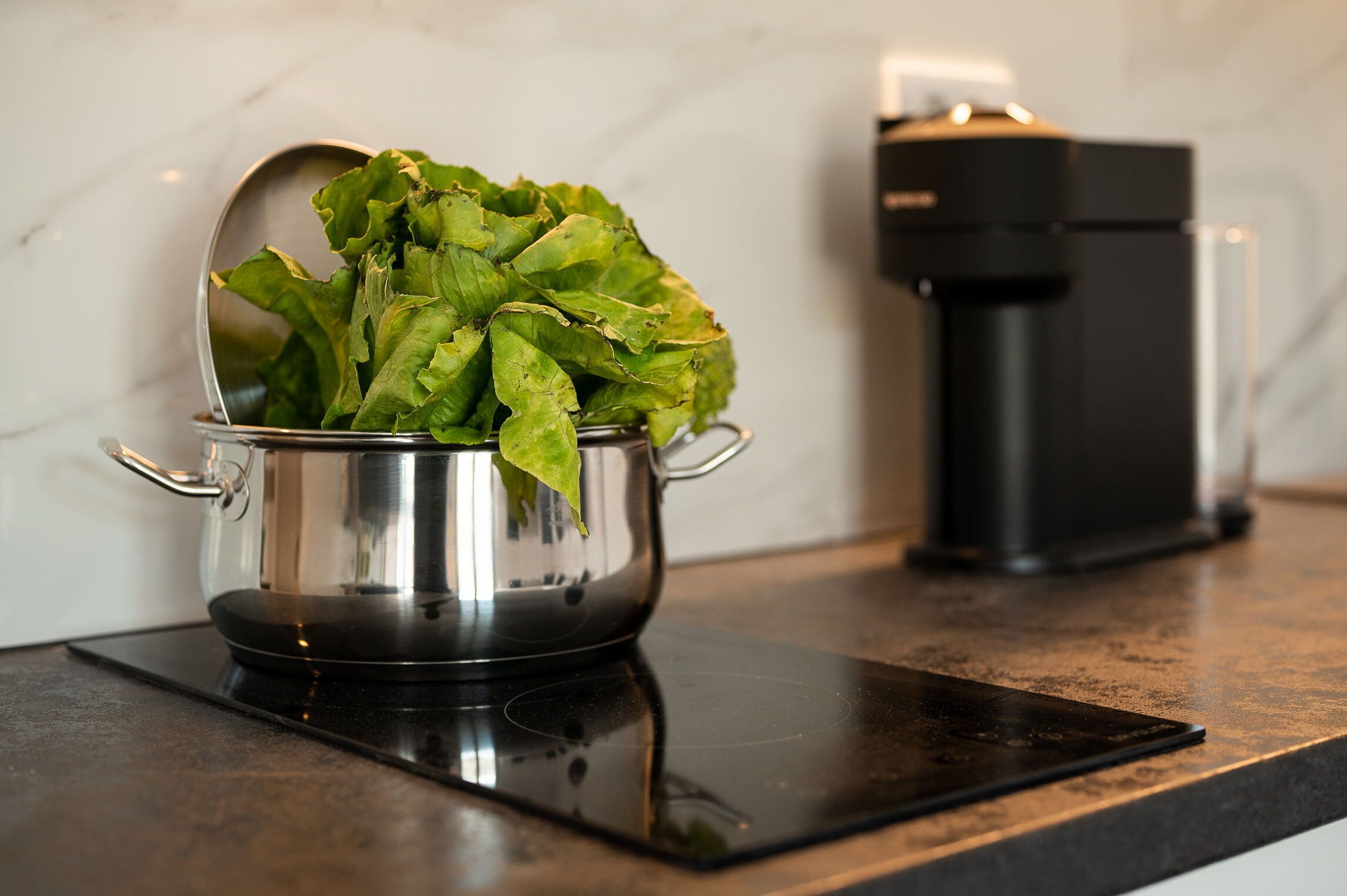 A stainless steel pot with fresh green lettuce on a black induction cooktop.