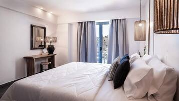 A hotel room with a large bed, a desk with a lamp, and a view of the outdoors through the window.