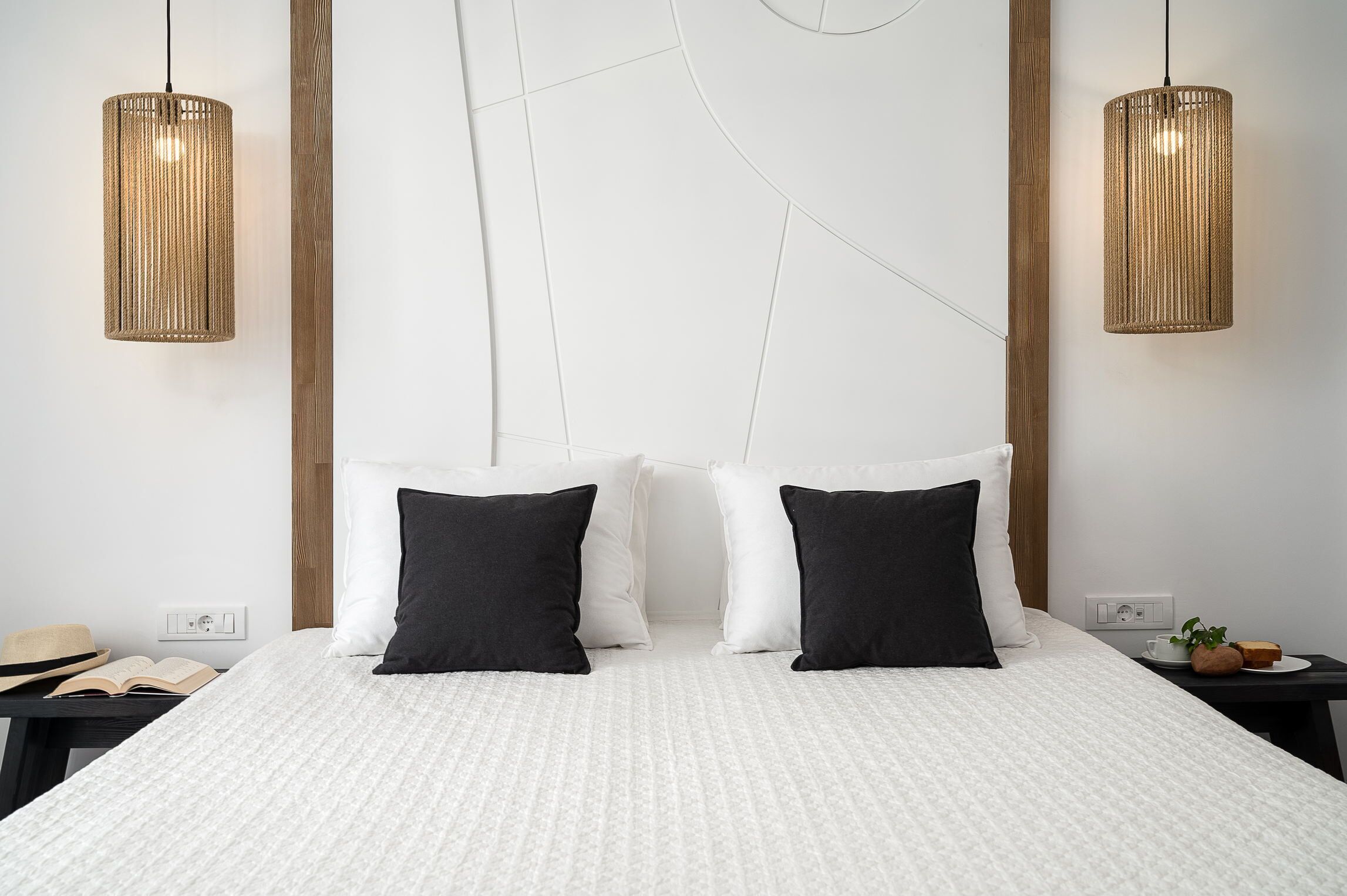 A modern hotel room with a large bed, two bedside tables, and two hanging pendant lights.