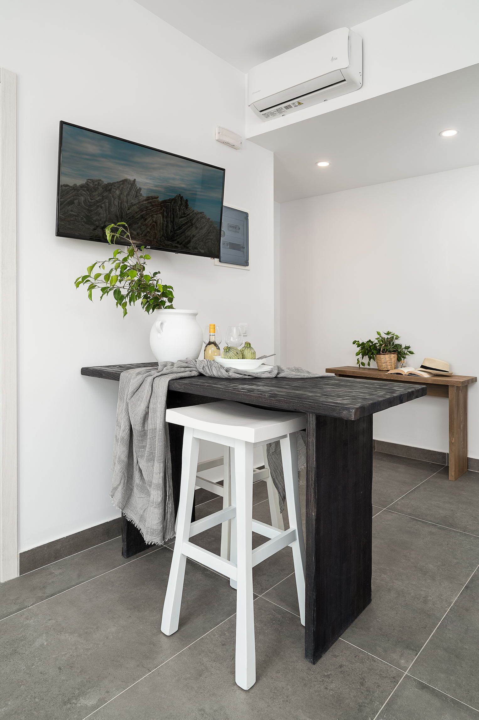 A modern kitchen with a central island, white bar stools, a mounted flat-screen TV, and a potted plant.