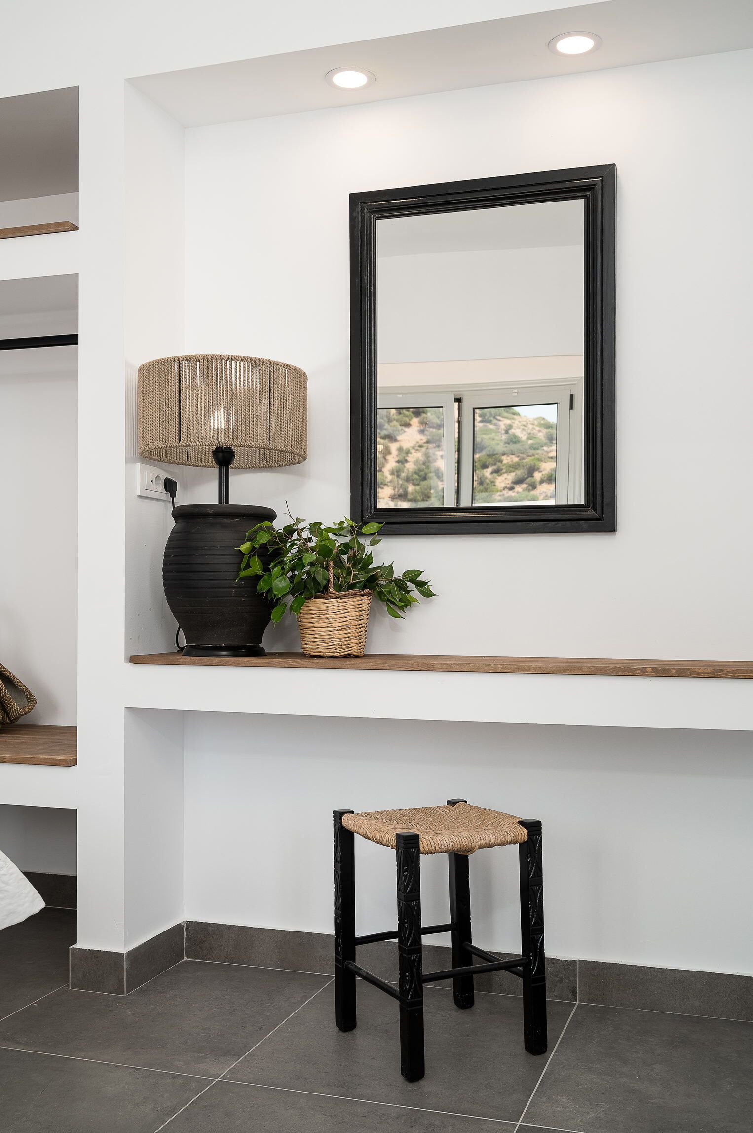 A modern bathroom with a large mirror, a floor lamp, a potted plant, and a wooden stool.