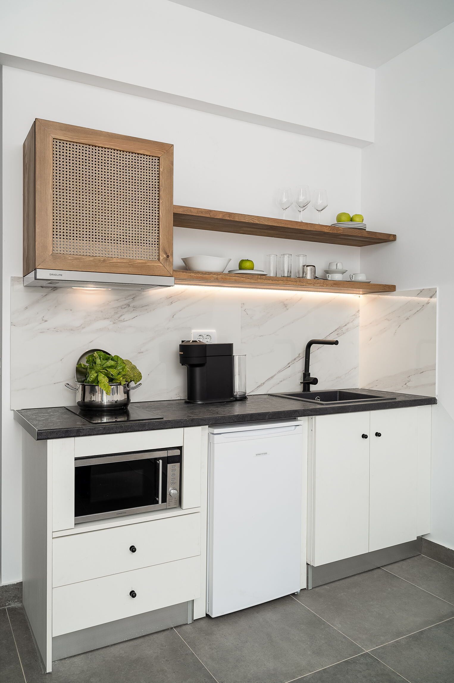 Una cocina moderna con armarios blancos, encimera negra, horno integrado, fregadero y repisa de madera arriba.