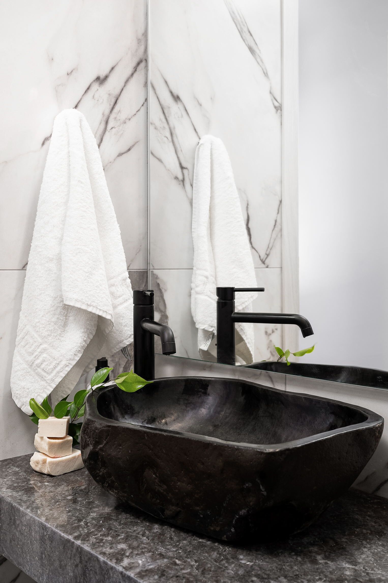 Un bagno con un lavandino in pietra nera, piastrelle in marmo bianco e due asciugamani bianchi appesi al muro.