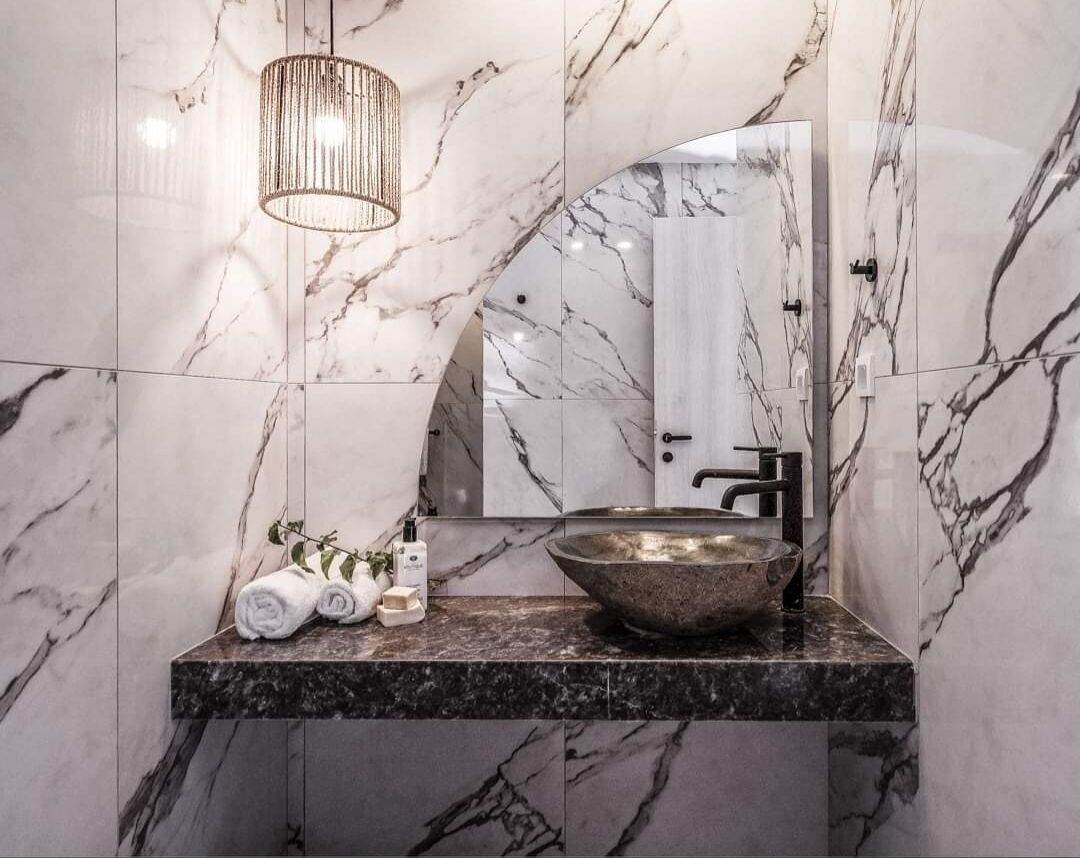 A bathroom with a marble vanity, a vessel sink, and a hanging light fixture.