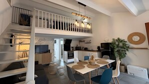 A modern interior with a dining area, kitchen, and upper-level balcony. - Maison au Cœur de La Palmyre (Les Mathes)