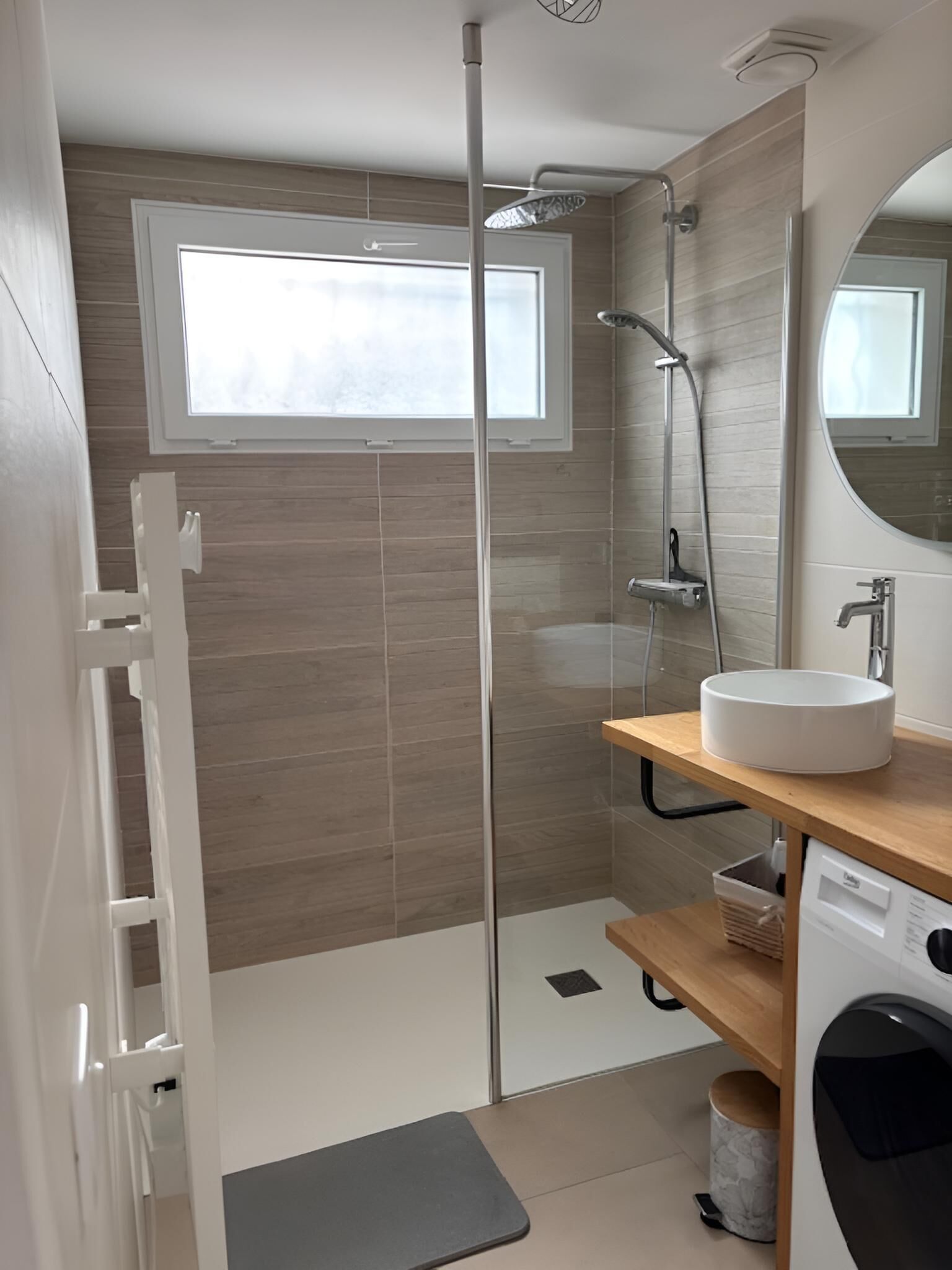 Un baño moderno con cabina de ducha de vidrio, lavabo empotrado y lavadora.