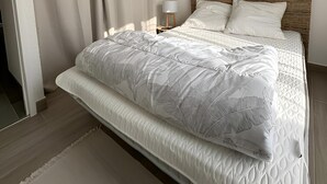 A modern bedroom with a large bed, a wooden headboard, and a hanging light fixture. - Maison au Cœur de La Palmyre (Les Mathes)