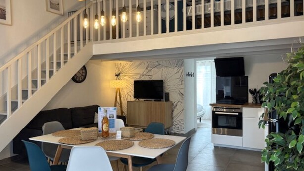 A modern kitchen with a dining area, a staircase, and a TV. - Maison au Cœur de La Palmyre (Les Mathes)