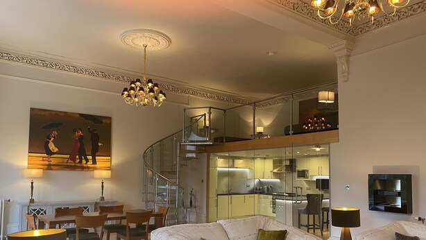 Un salon moderne comprenant un canapé, des fauteuils, une table à manger, un escalier et un coin cuisine.