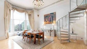 Un coin repas avec une table dressée pour quatre personnes, un lustre et un escalier doté d’une rampe en verre.
