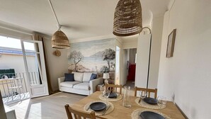 Un comedor con una mesa de madera dispuesta para cuatro personas, dos lámparas colgantes de mimbre, un sofá y un mural en la pared.