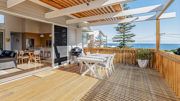 Une terrasse en bois avec un espace repas, un barbecue et une vue sur la mer.