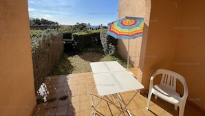 A patio with a white table and chair, a colorful umbrella, and a view of a garden and hills.