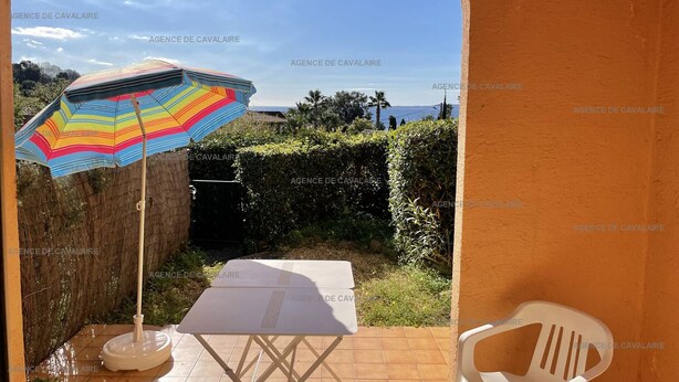 A patio area with a table and chairs, a colorful striped umbrella, and a view of the sea through a window.