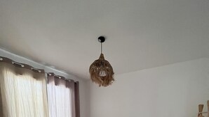 A bedroom with a bed, curtains, a hanging light fixture, and a wooden chair. - Maison de Vacances à 15 Km de Saint-jean de Mont (Sallertaine)