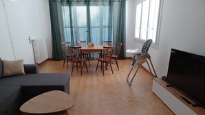 A modern living room with a sofa, a dining table with chairs, a TV, and a wheelchair. - Maison de Vacances à 15 Km de Saint-jean de Mont (Sallertaine)
