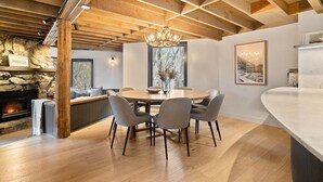 A modern dining area with a round table, grey chairs, and a stone fireplace. - Alpine Uralla - Dinner Plain (Dinner Plain)