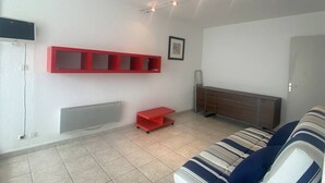 Una sala de estar con un sofá, una estantería roja, un radiador y un cuadro enmarcado en la pared.