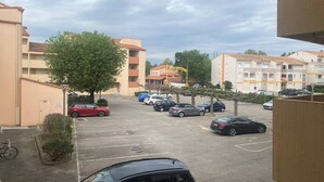 Un estacionamiento con varios coches, un árbol y edificios de apartamentos al fondo.