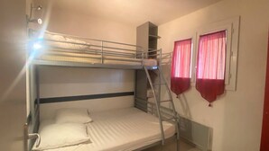 Habitación con literas, una escalera, una ventana con cortinas rojas y un radiador.