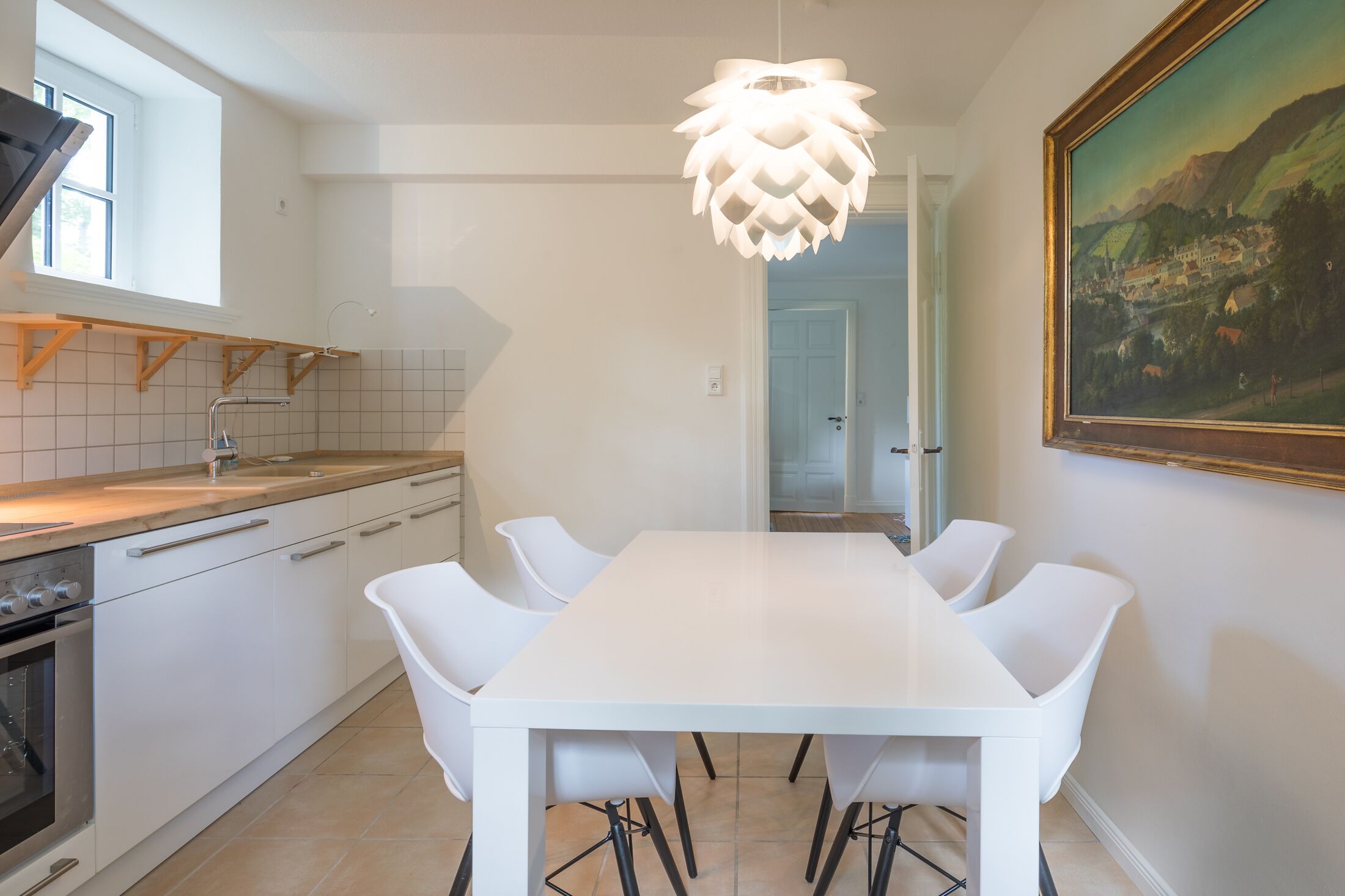 A modern kitchen with white cabinetry, a large island, and a dining area with a white table and chairs.