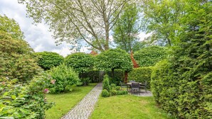 A garden with a cobblestone path leading to a seating area surrounded by lush greenery and a large tree.