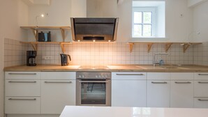 A modern kitchen with white cabinetry, a built-in oven, a coffee maker, and a window providing natural light.