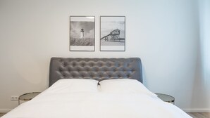A neatly made bed with a tufted headboard, two bedside tables, and two framed pictures on the wall.
