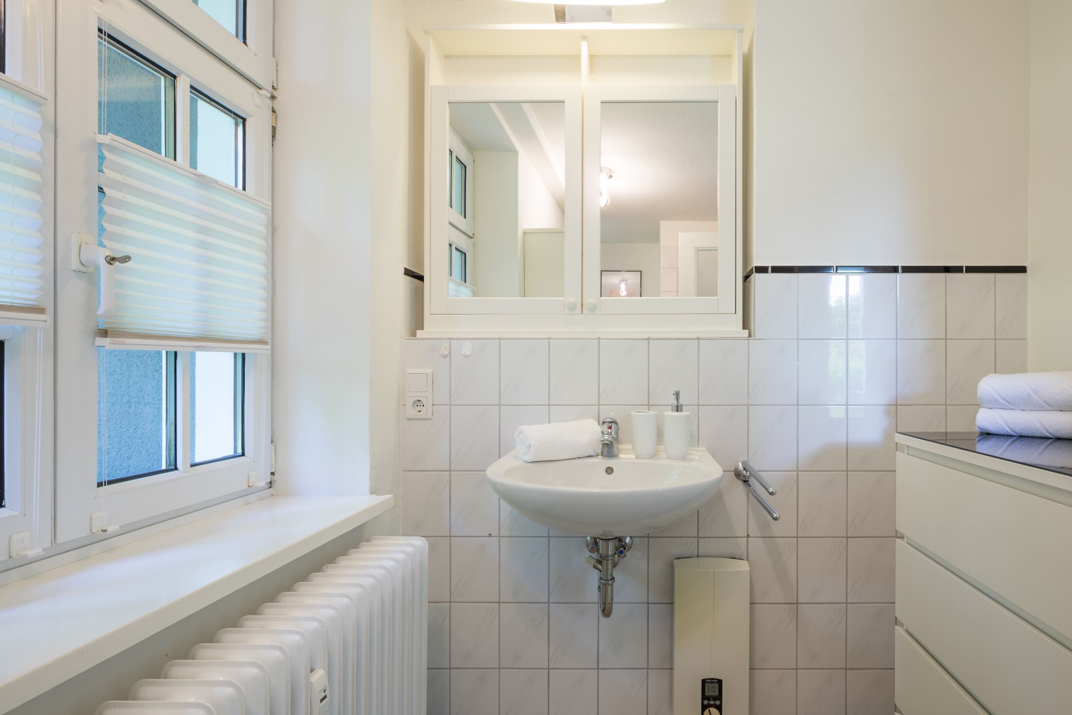 A bathroom with a window, a sink, a mirror, and a towel rack.