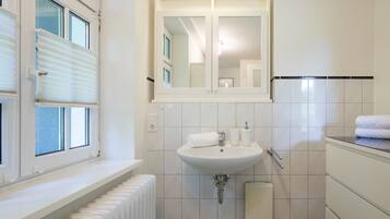 A bathroom with a window, a sink, a mirror, and a towel rack.