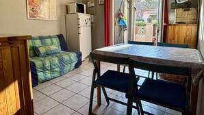 Una habitación compacta con una mesa de comedor y sillas, un sofá, un refrigerador y una televisión.