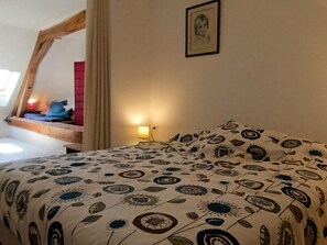 Quarto com cama, mesa de cabeceira, abajur, janela com cortinas e um quadro na parede.