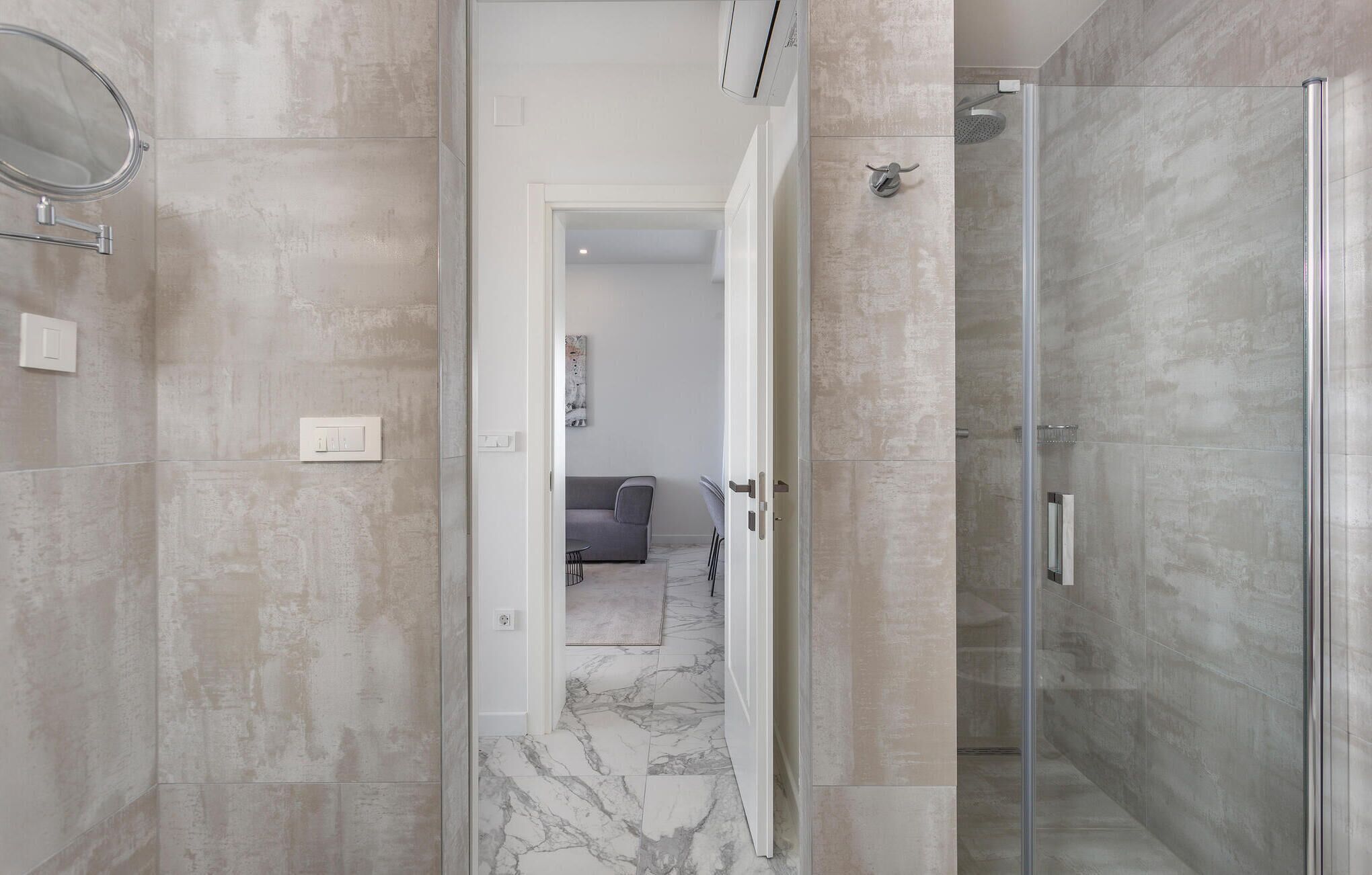 A modern bathroom with a glass shower enclosure, marble flooring, and a visible door leading to another room.